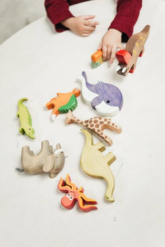 A child plays with a variety of colorful wooden animal toys on a white table indoors.